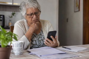 Idosa consulta celular e documentos para verificar a situação do BPC suspenso ou bloqueado.